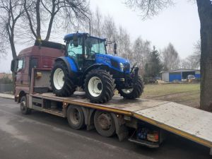 Niebieski ciągnik New Holland na pojeździe transportującym